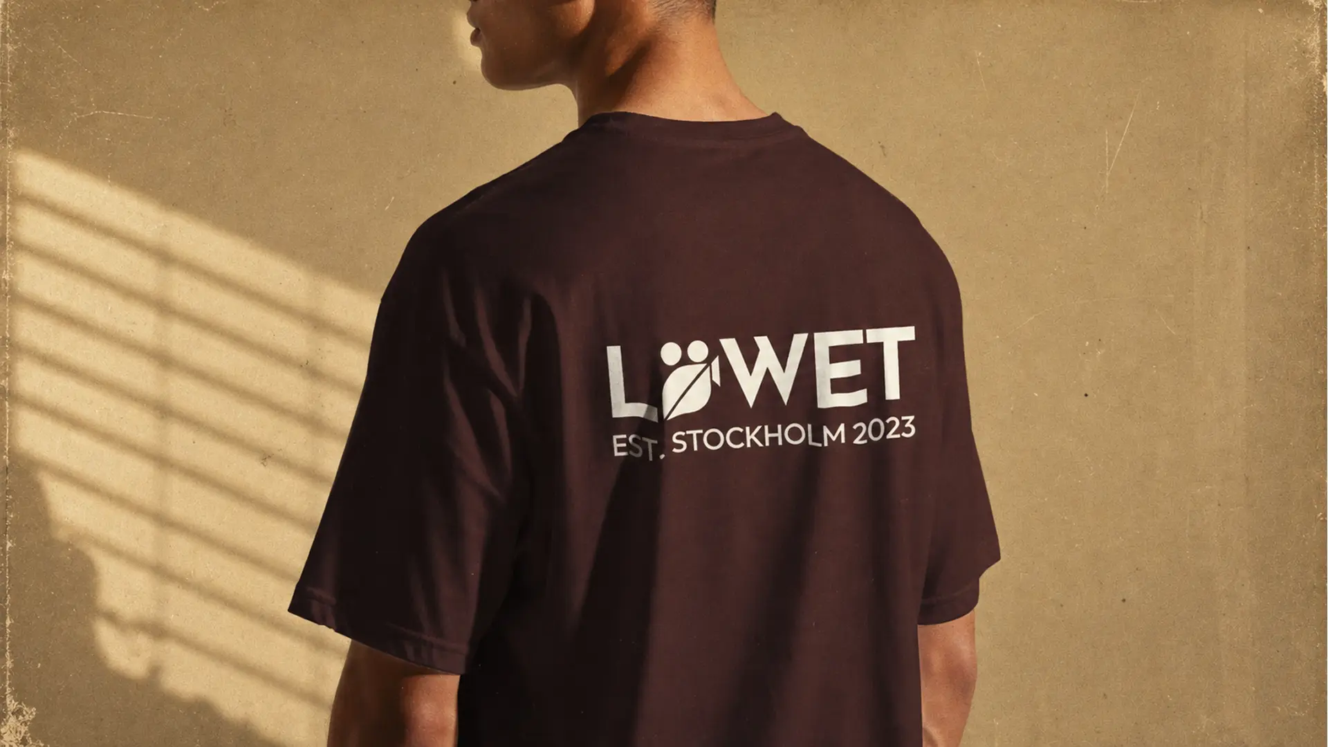 Löwet T-shirt i mörkbrunt med off-white tryck på ryggen, sett bakifrån i solsken